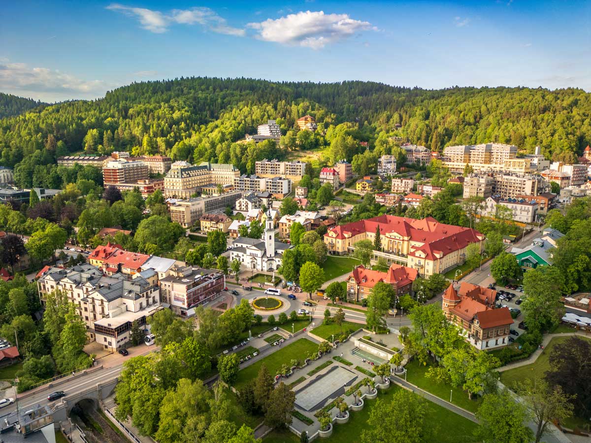 Widok z drona na otoczone zielenią budynki uzdrowiskowe w centrum Krynicy-Zdroju.