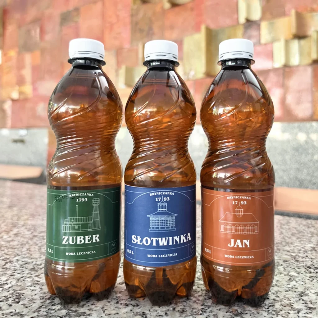 kryniczanka-3-butelki-wod-leczniczych trzy plastikowe butelki wód leczniczych o pojemności 0,5 litra stojące na marmurowym blacie na tle ceramicznych kafelków w Pijalni Głównej w Krynicy-Zdroju