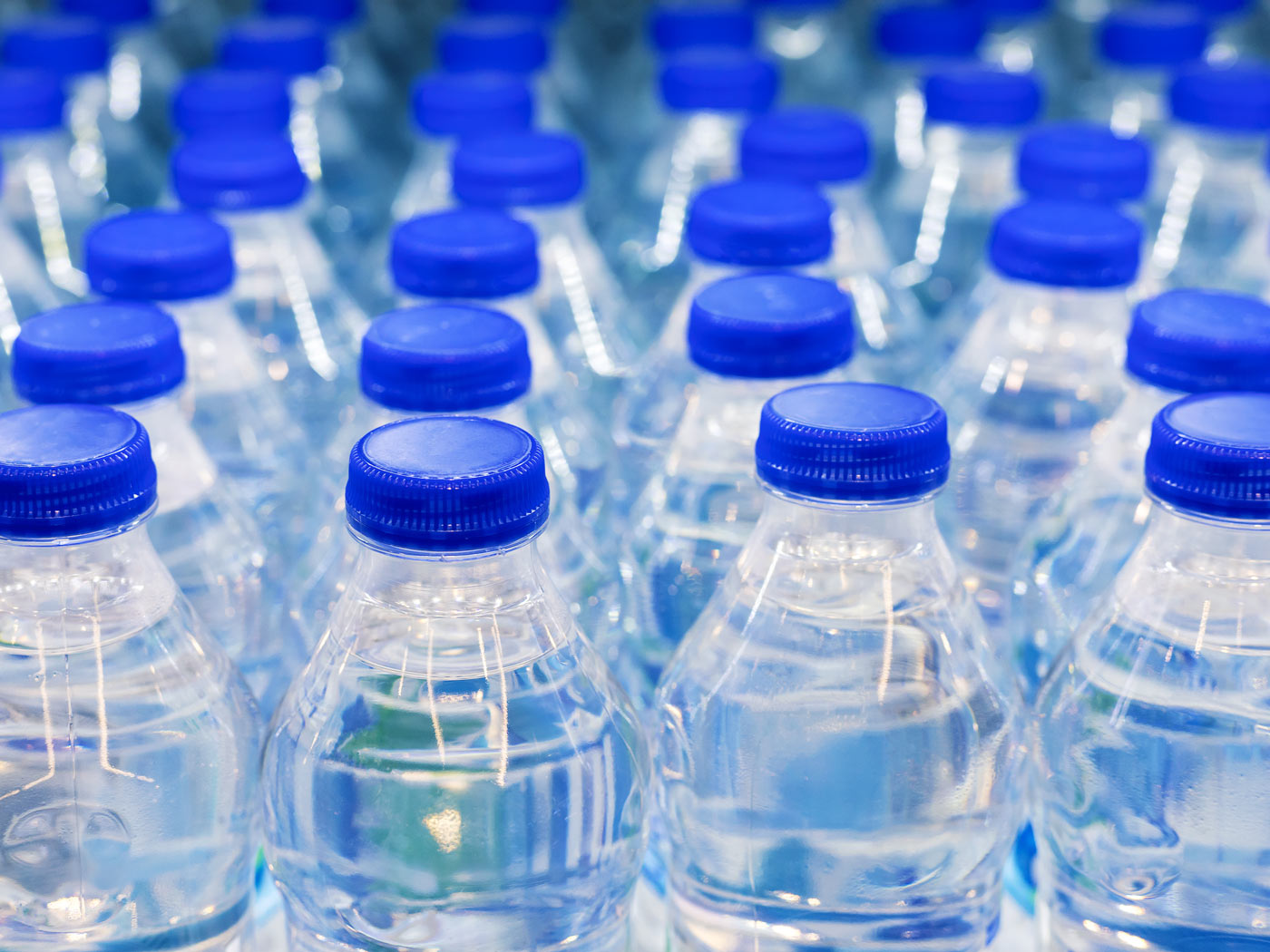 Rzędy plastikowych butelek wody mineralnej z niebieskimi zakrętkami.